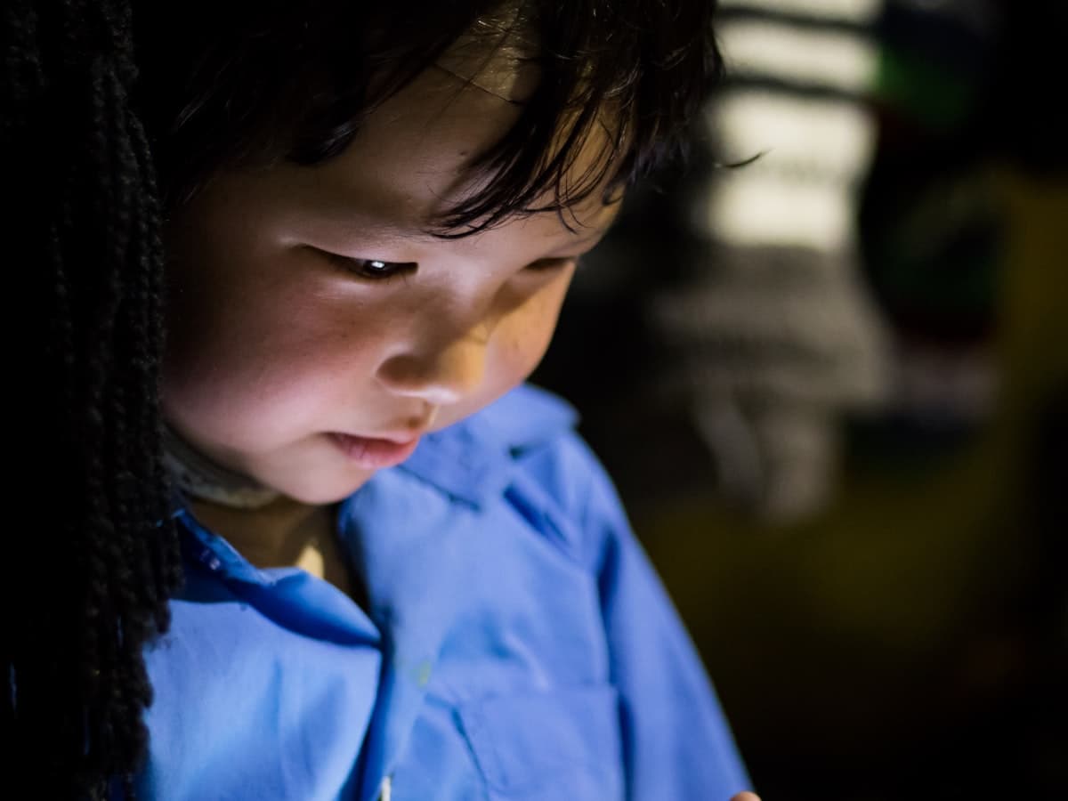 A young child's face lit by the glow of a tablet screen