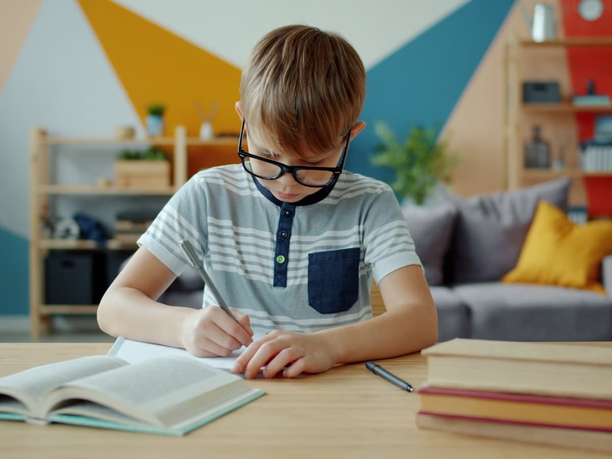 A focused student writing at a desk with books and no screen in sight
